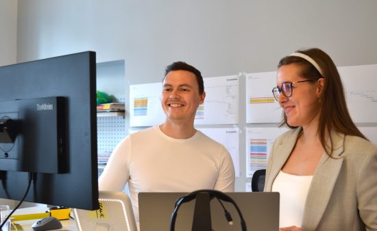 Two people sitting at a desk and looking at a monitor in a modern office.